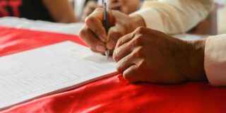 Hands of an older man signing a piece of paper.