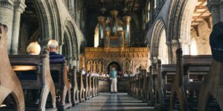 People sitting on a pew in a large stone church.