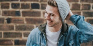 A young man wearing a beanie hat in front of a brick wall.