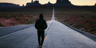 Male teen seen walking away from the camera a desert road.