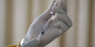 Hands holding a vaccine vial and syringe.