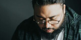 A Latino looking man wearing glasses has his head bowed.