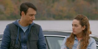 Ralph Macchio and Mary Mouser from The series Cobra Kai stand talking by a car in a screen capture.