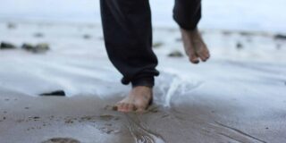 A man's feet are seen close up running through sand at the beach.