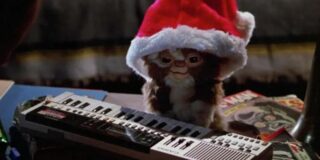 A Gremlin wears a Santa hat and sits at a piano keyboard.