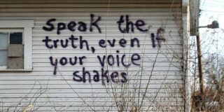 An abandoned building with "Speak the truth, even if your voice shakes" spray painted on the side.