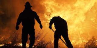 The silhouettes of 2 firefighters working a fire line are shown with flames as the background.