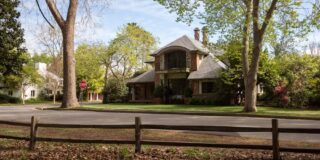 A nice European style two story house with fancy brick work and wrought iron fencing is seen from the road.