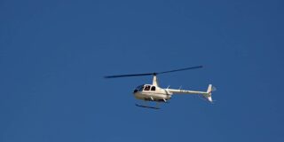 A commercial helicopter is shown high up against a blue sky.