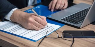 A man in a suit sits at a laptop filling out paperwork.