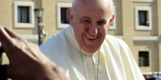 Pope Francis is shown outside facing a crowd and smiling.