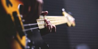 A guitar being played is seen close up from it's widest end with the players strumming hand out of focus and their fret hand in focus.