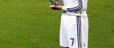 Soccer player Cristiano Ronaldo is seen on the field in a white uniform and holding a ball trophy.