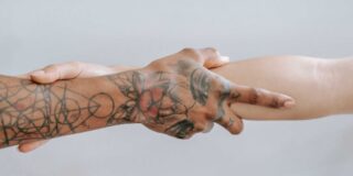 A tattooed hand and forearm is shown grabbing the forearm of a non-tattooed arm.