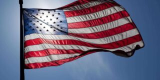 American flag waving in the wind with the sun shining through it.