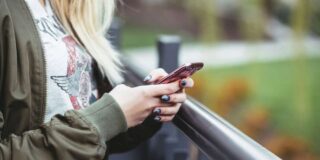 I woman stands outside holding her phone.