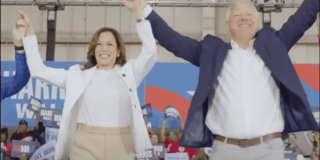 VP Kamala Harris and Tim Walz raise clasped hands in front of a crowd.