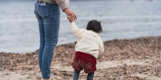 Woman holding a toddler's hand on the beach.