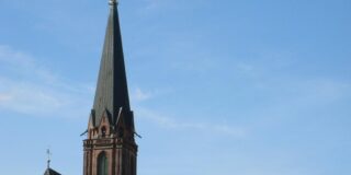 An old church steeple seen over a red tile roof.