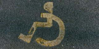 Worn yellow handicap symbol painted on asphalt.