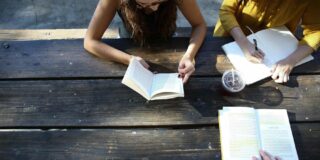 A group of people sitting at a picnic table reading books.