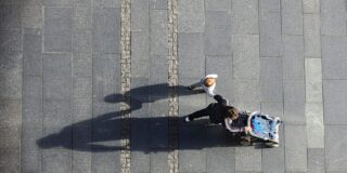 A woman is seen from high above pushing a stroller and holding a toddler's hand.