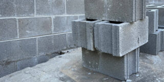 Four grey cinder blocks, stacked in front of a cinder block wall.