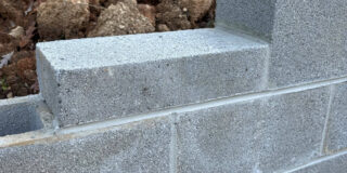 The top of a partially complete grey cinder block wall with dirt piled behind it.