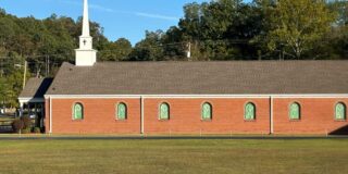 Side view of a one story red brick church with a white steeple.