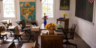 A historic classroom as seen from the side with student and a teacher's desk.