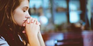 A woman has her hands folded in prayer.