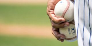 A man's hand is shown closeup against his uniformed leg holding two baseballs at his side.