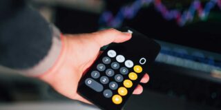 A person holds a calculator set at zero with an out of focus graph in the background.