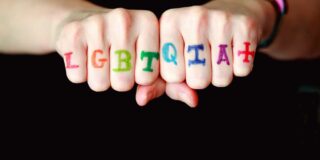 LGBTQIAH+ Written across someone's fingers.